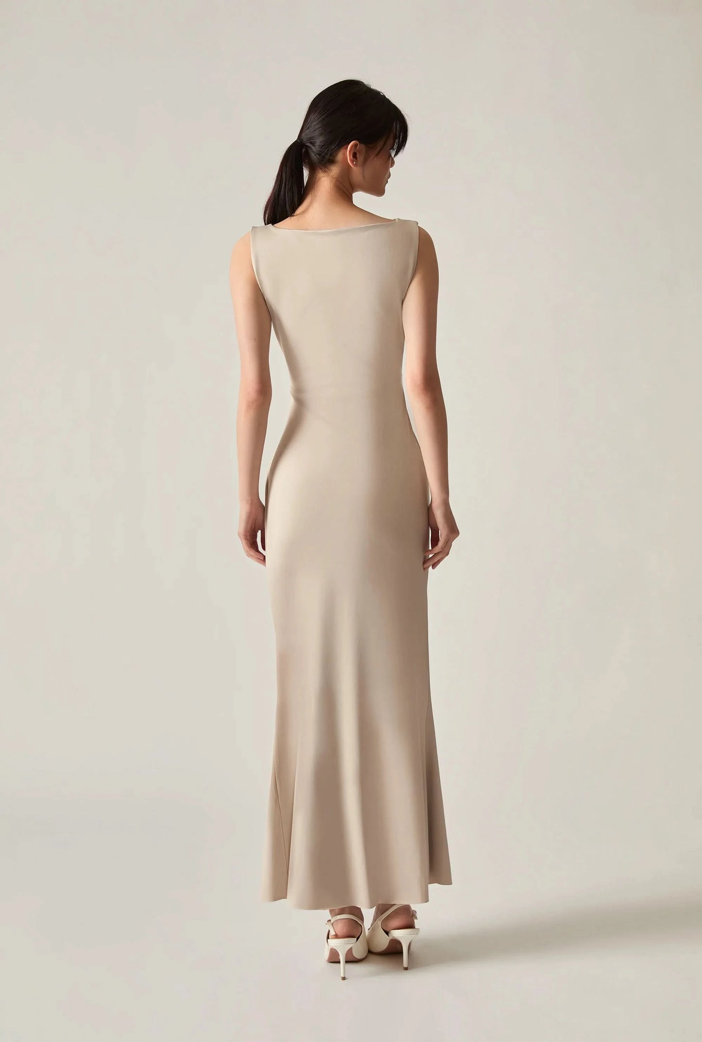 Woman wearing a plain beige sleeveless dress, photographed from the back against a soft beige background