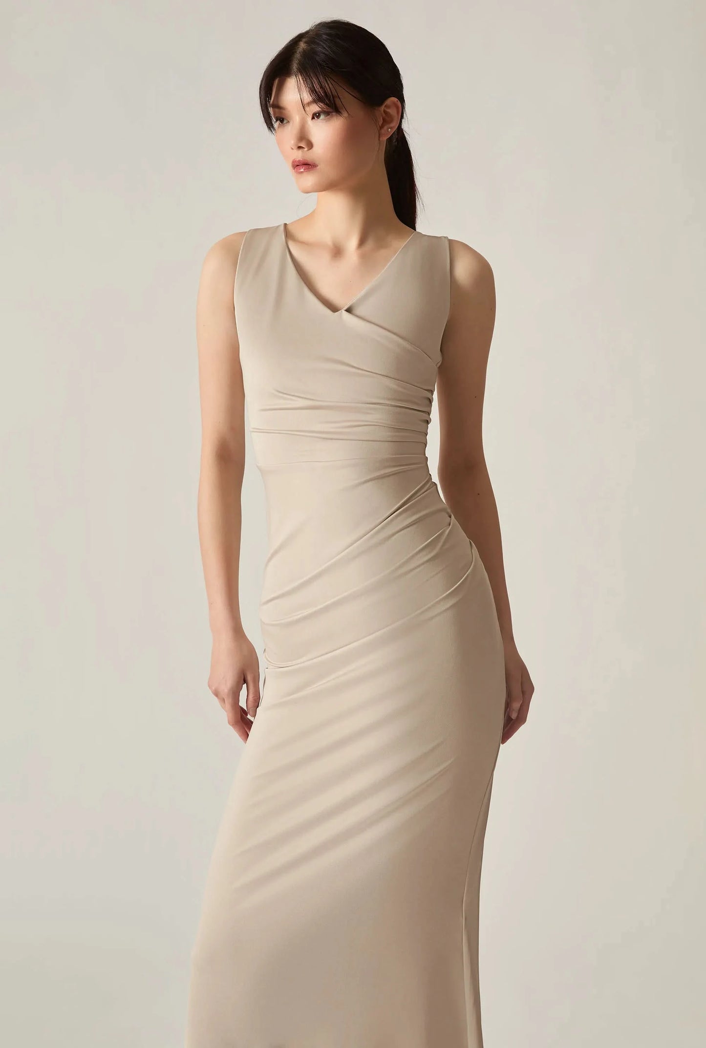 Close‑up front shot of a beige sleeveless dress on a soft beige background, highlighting fabric and detail.