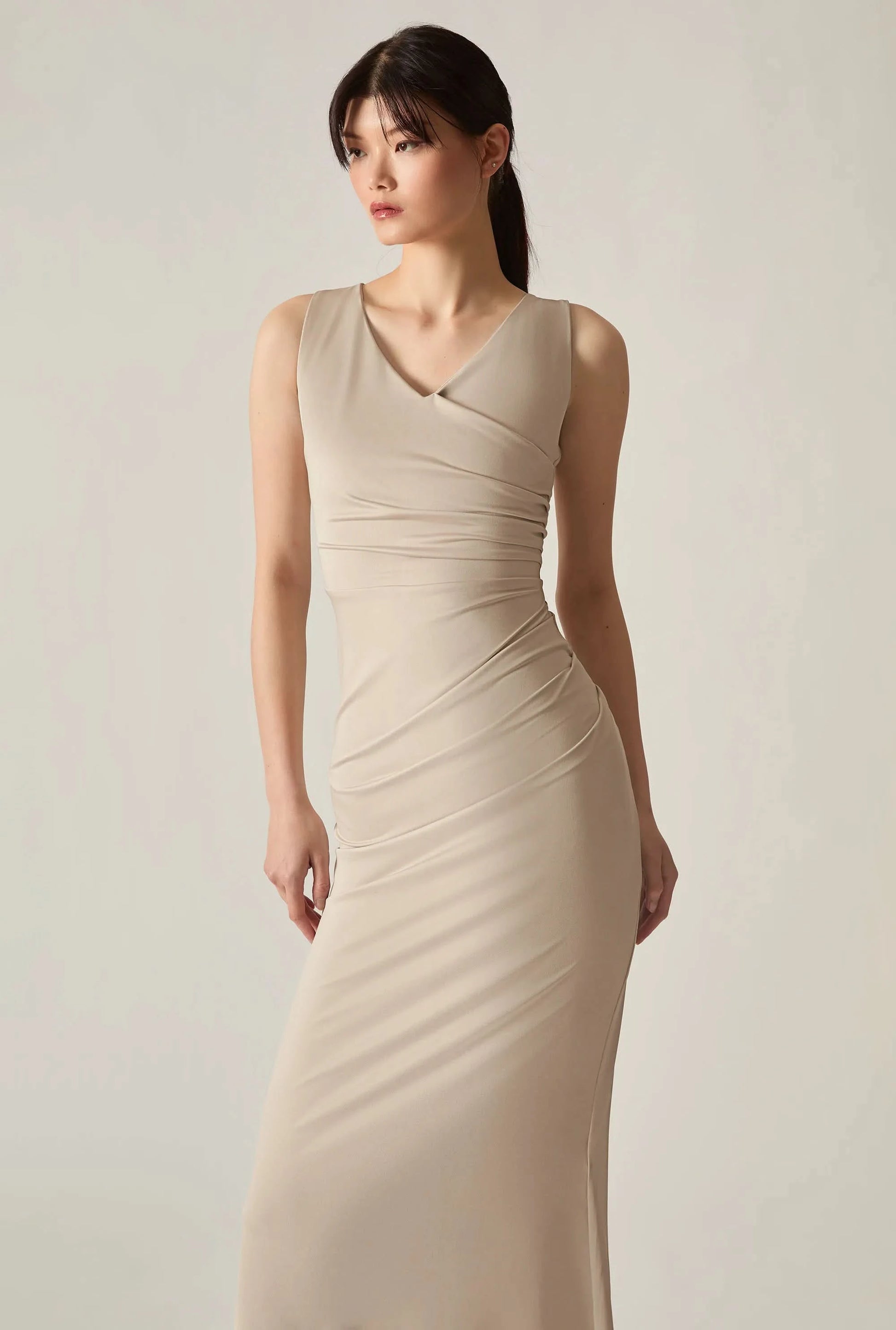 Close‑up front shot of a beige sleeveless dress on a soft beige background, highlighting fabric and detail.