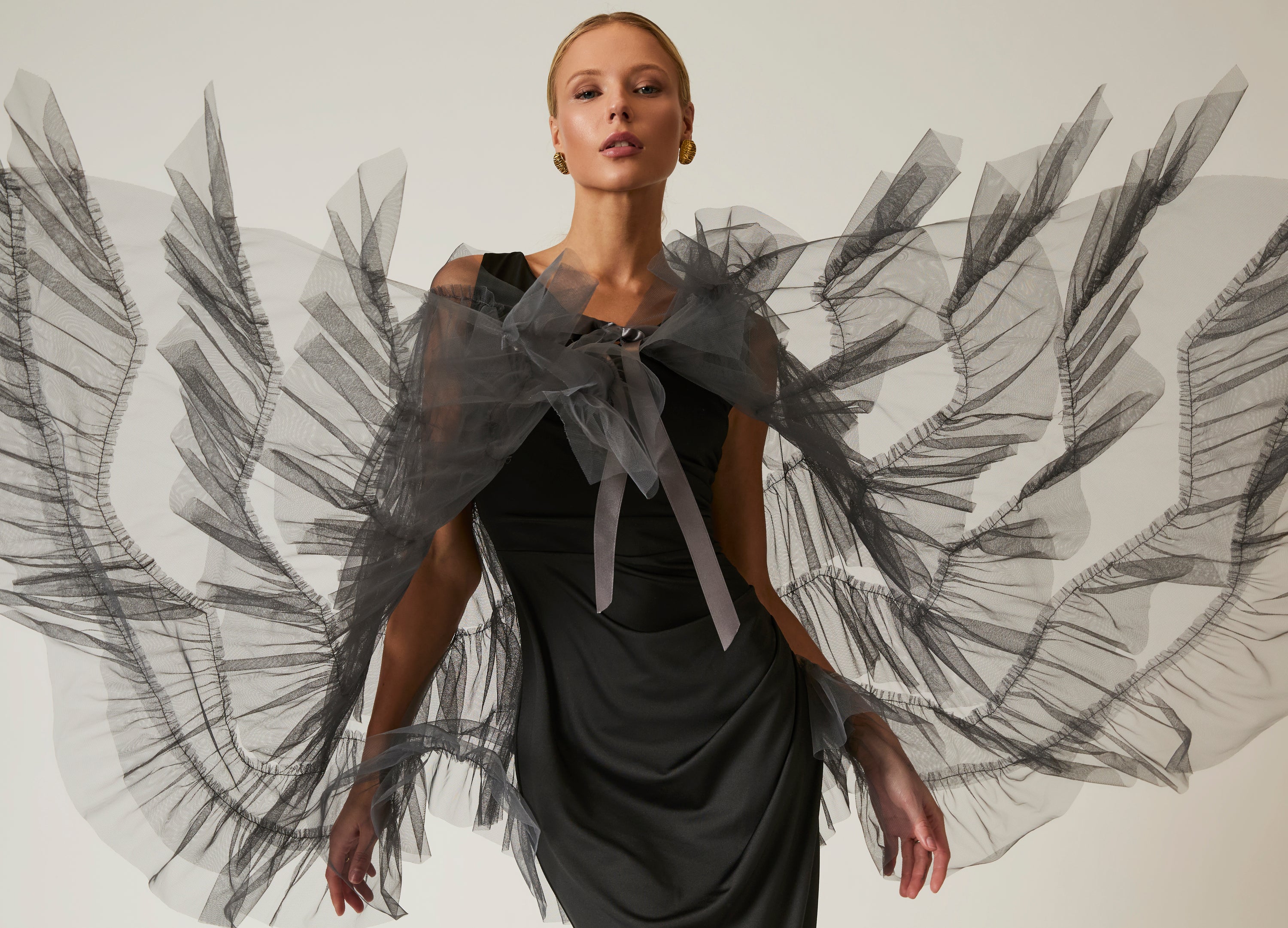 Woman wearing a black dress with sheer, fan-like sleeves against a neutral background