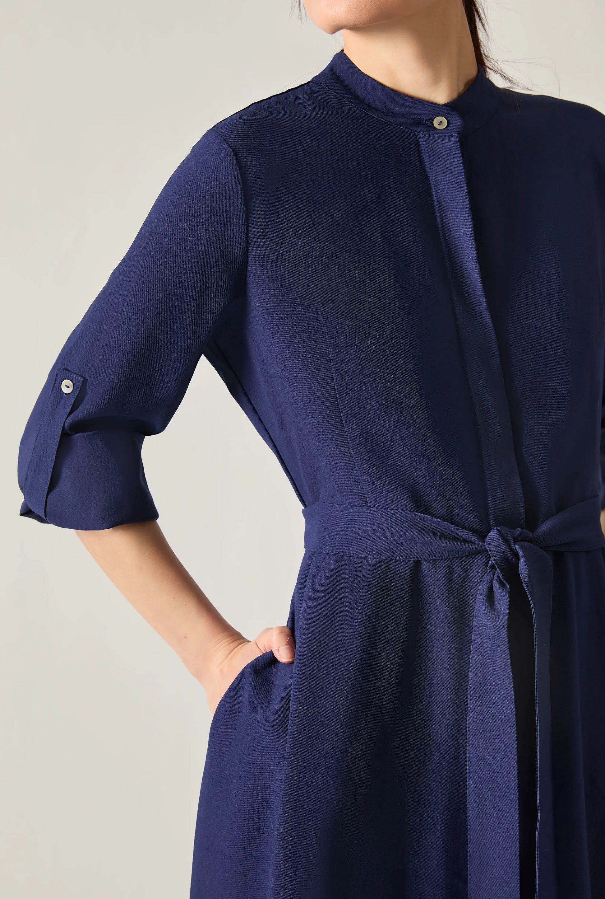 Close‑up of the sleeve and belt detail on the navy tie‑waist midi dress against a soft beige background.