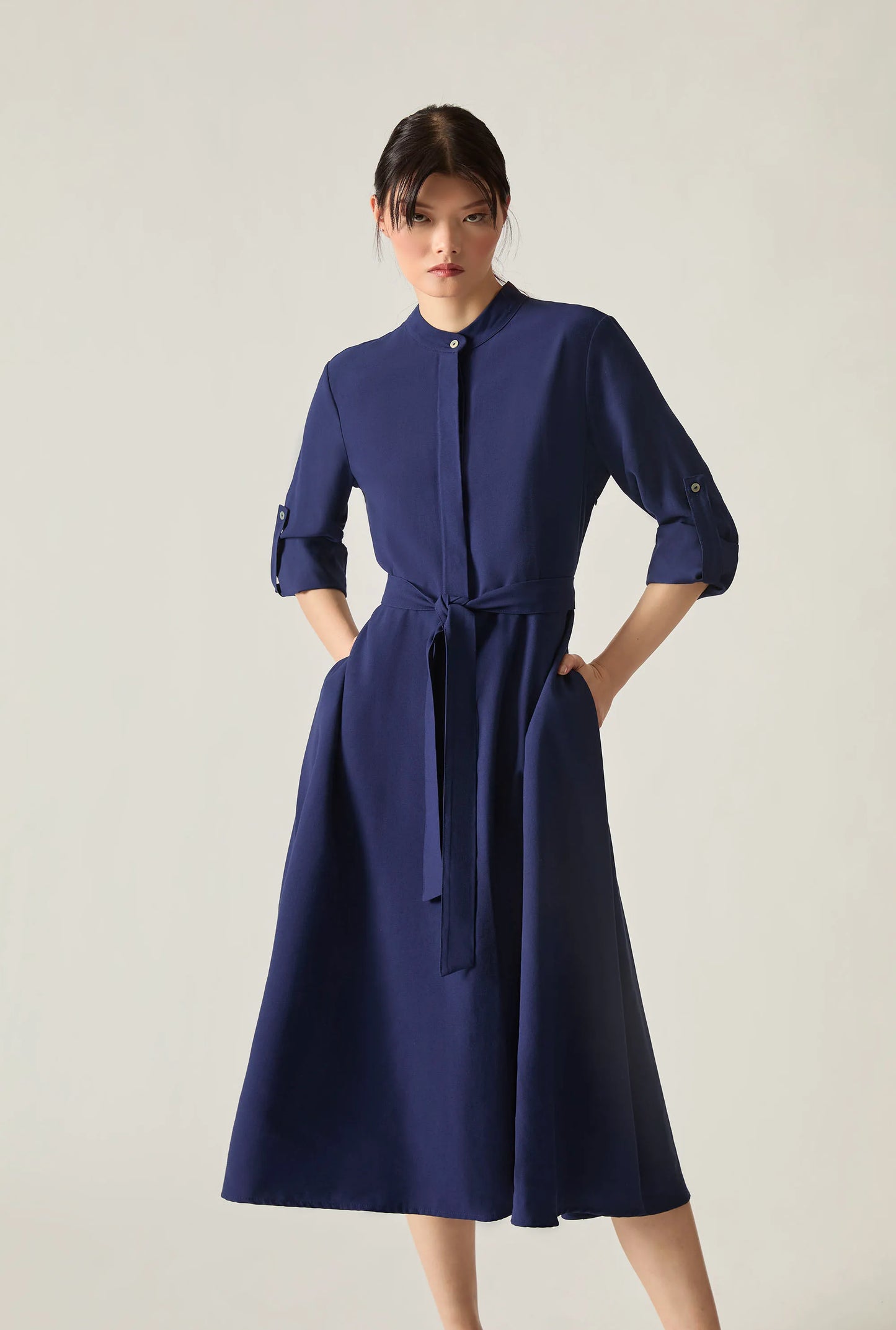 Close‑up full‑body view of a navy tie‑waist midi dress on soft beige background.