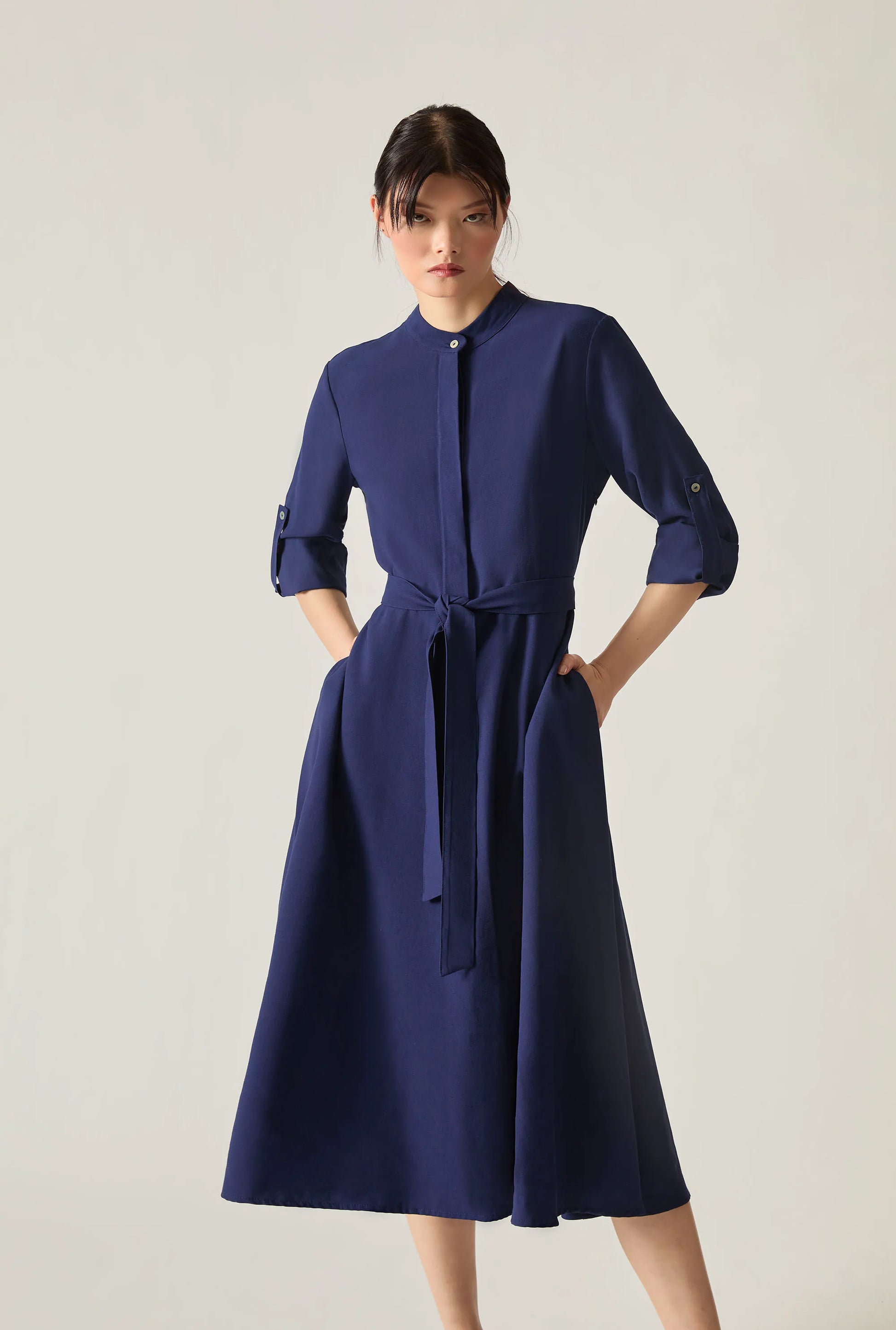 Close‑up full‑body view of a navy tie‑waist midi dress on soft beige background.