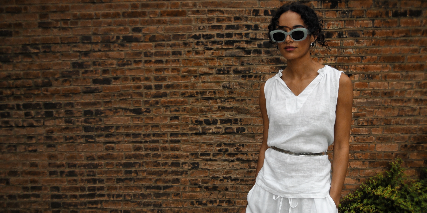 Model wearing an elegant white linen outfit by James Lakeland against a textured brick wall